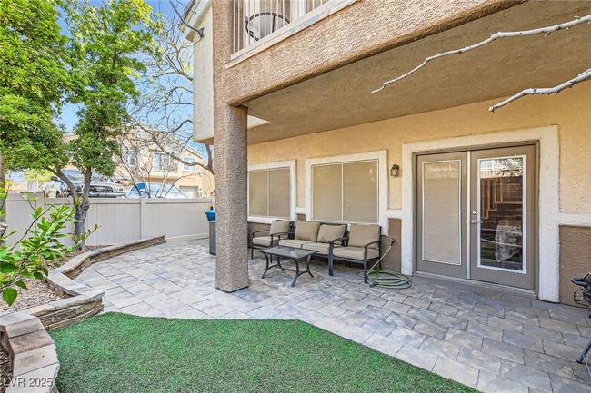 View of the back patio & terrace with wall/fence enclosed covered patio area with pavers, artifical turf and established landscaping at 7143 Cabin Fever St Unit 102 | Image 20