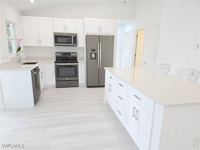 Kitchen with stainless steel appliances, a sink, light wood finished floors, white cabinets, and vaulted ceiling | Image 9