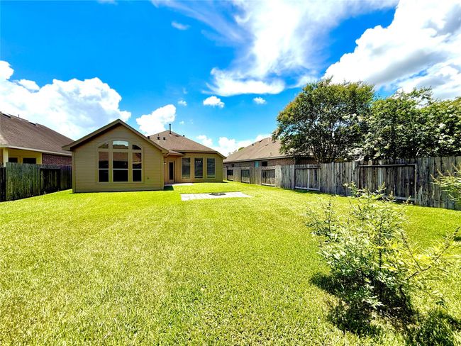 Spacious backyard with well-maintained lawn, bordered by a wooden fence, and featuring a house with large windows. Ideal for outdoor activities and enjoying sunny days. | Image 24