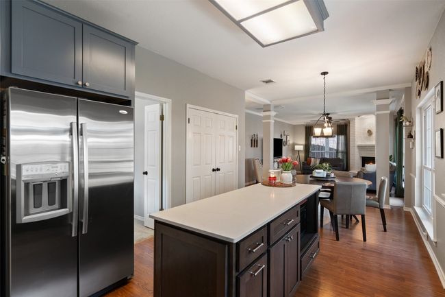 Kitchen featuring dark wood-style flooring, light countertops, stainless steel refrigerator with ice dispenser, and a brick fireplace | Image 12