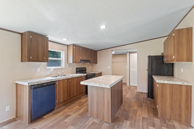 Kitchen with dishwasher, freestanding refrigerator, black range with electric cooktop, light countertops, and wood finished floors | Image 11