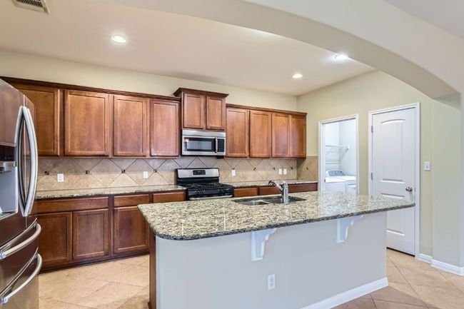 Kitchen with appliances with stainless steel finishes, washing machine and dryer, light stone countertops, a kitchen island with sink, and recessed lighting | Image 12