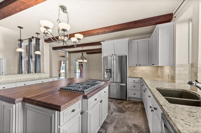 Kitchen featuring stainless steel appliances, butcher block countertops, a chandelier, backsplash, and beam ceiling | Image 9