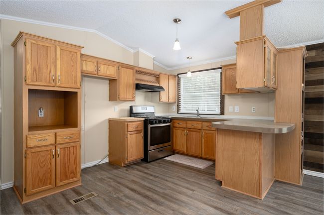 Kitchen featuring stainless steel range with gas cooktop, vaulted ceiling, under cabinet range hood, ornamental molding, and dark wood-style flooring | Image 24