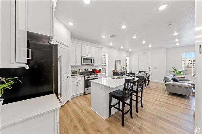 Kitchen featuring appliances with stainless steel finishes, a breakfast bar area, white cabinets, light wood-style floors, and recessed lighting | Image 11