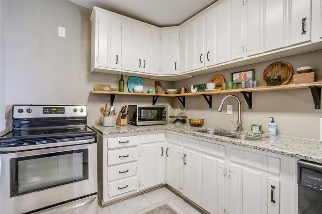 Kitchen with stainless steel appliances, open shelves, light tile patterned floors, and white cabinetry | Image 9