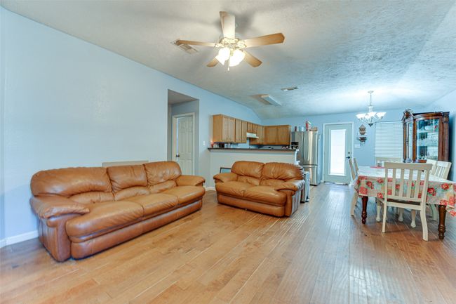Living area with lofted ceiling, light wood finished floors, visible vents, baseboards, and ceiling fan with notable chandelier | Image 16