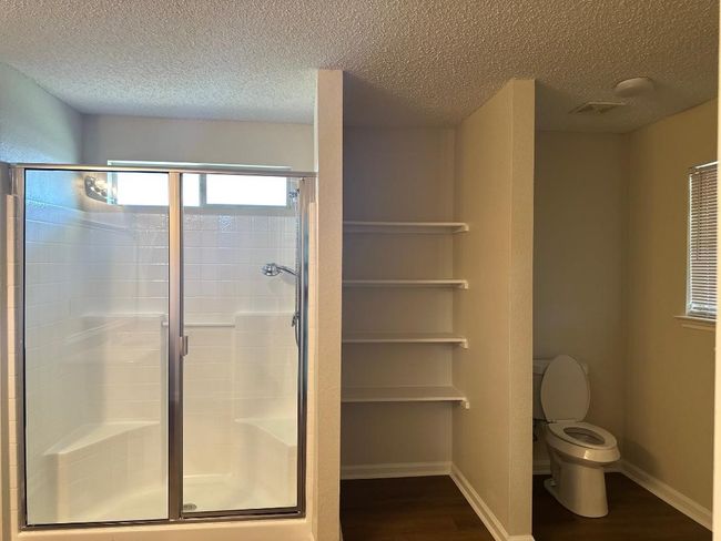 Full bathroom with wood finished floors, a textured ceiling, a shower stall, toilet, and baseboards | Image 11