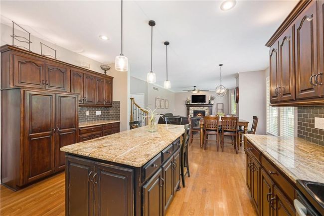 Kitchen featuring a stone fireplace, decorative backsplash, light wood finished floors, light stone counters, and open floor plan | Image 15