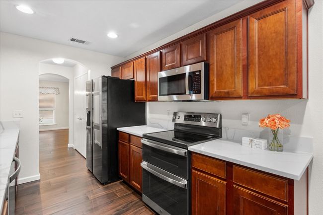 Kitchen with appliances with stainless steel finishes, arched walkways, dark wood tile flooring, light countertops, and recessed lighting | Image 7