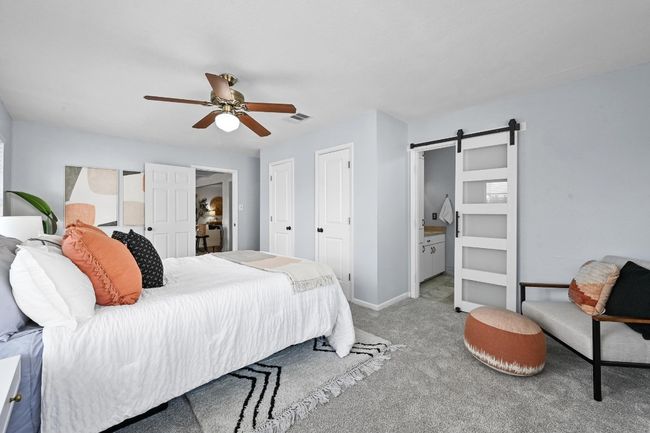 Carpeted bedroom with a barn door, baseboards, connected bathroom, and ceiling fan | Image 6