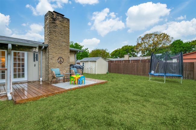 View of yard featuring a deck, a trampoline, a fenced backyard, an outdoor structure, and a storage unit | Image 25