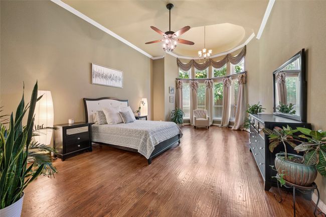 Bedroom featuring wood finished floors, crown molding, a high ceiling, a chandelier, and ceiling fan | Image 20