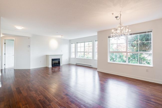 Unfurnished living room with a chandelier, a glass covered fireplace, dark wood-style floors, and a baseboard radiator | Image 9