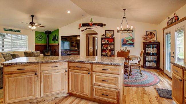 Kitchen featuring a wood stove, vaulted ceiling, light brown cabinetry, open floor plan, and ceiling fan | Image 13