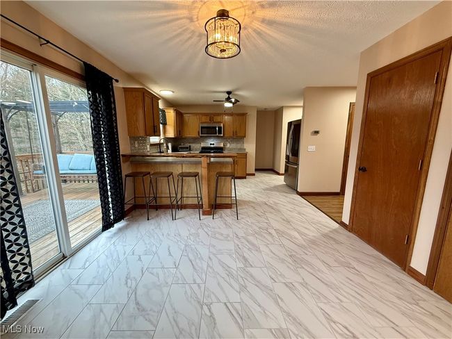Kitchen featuring stainless steel appliances, light marble finish flooring, brown cabinets, a peninsula, and decorative backsplash | Image 10