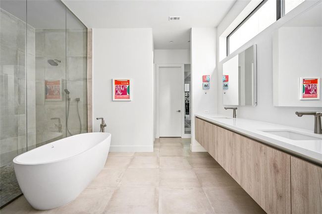The serene primary bath features a freestanding soaking tub, walk-in shower with dual shower heads, and a long double vanity with floating cabinetry. Clean lines and neutral tones create a calming retreat, while the clerestory window invites soft natural light into the space. | Image 19