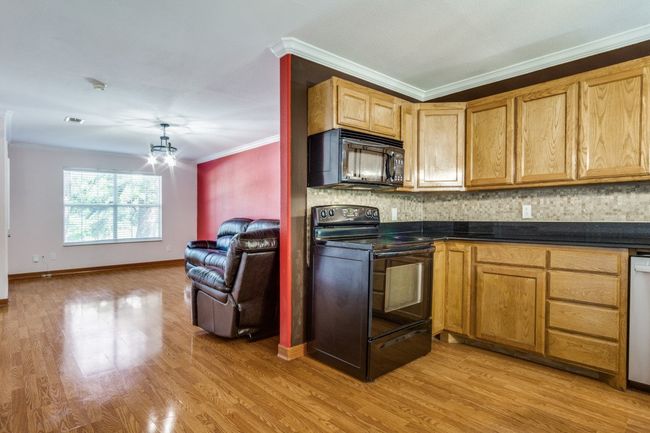 Kitchen with black appliances, ornamental molding, backsplash, dark countertops, and light wood-style flooring | Image 10