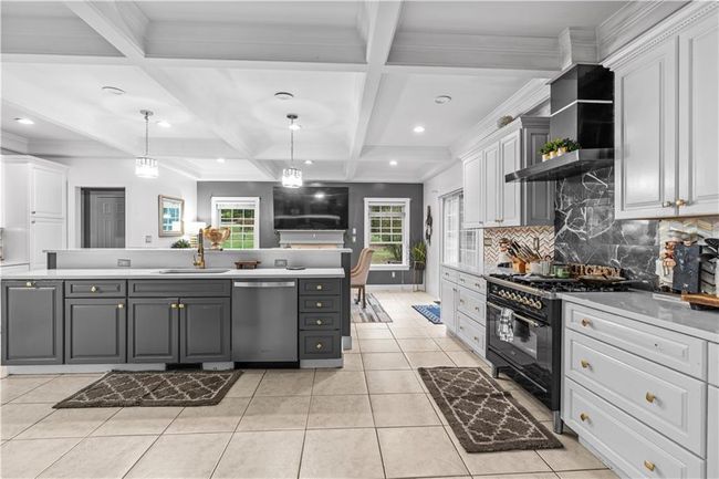 Kitchen featuring stainless steel dishwasher, high end black range, gray cabinetry, white cabinets, and backsplash | Image 6