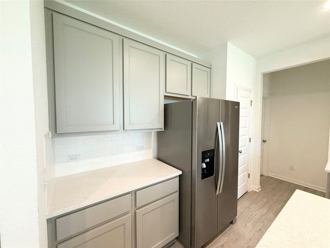 Kitchen featuring stainless steel refrigerator with ice dispenser, light wood-style flooring, backsplash, light stone countertops, and gray cabinets | Image 13