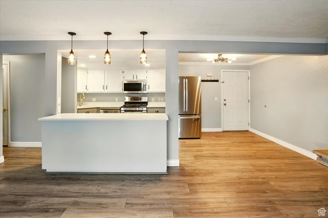 Kitchen featuring stainless steel appliances, white cabinets, light countertops, baseboards, and ornamental molding | Image 6