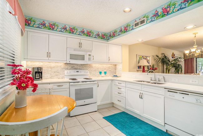 Kitchen with white appliances, updated cabinets, quartz countertops, textured tile backsplash, new double sink embedded in the newer quartz countertop. | Image 8