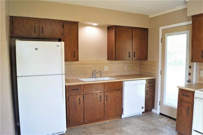 Kitchen featuring white appliances, light countertops, backsplash, crown molding, and brown cabinets | Image 4