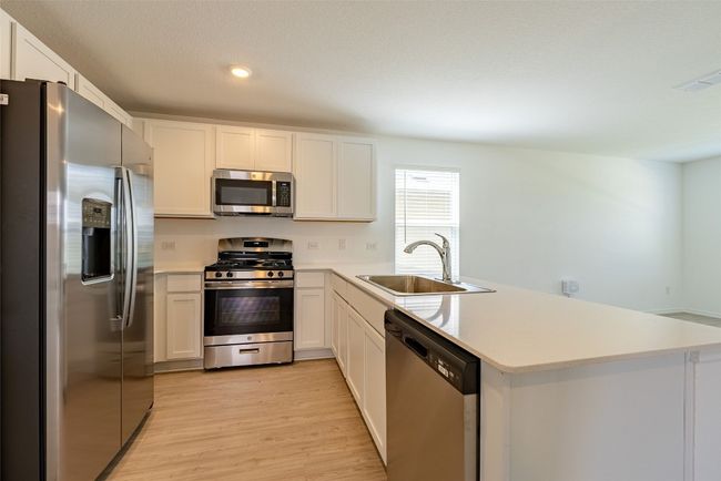 Kitchen featuring stainless steel appliances, a sink, a peninsula, light wood-style floors, and light countertops | Image 6