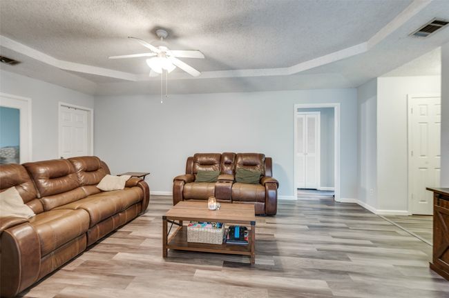 Living area with light wood-type flooring, ceiling fan, a textured ceiling, and a tray ceiling | Image 4