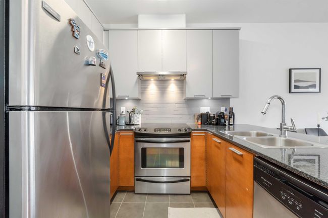 Kitchen featuring light tile patterned floors, under cabinet range hood, a sink, appliances with stainless steel finishes, and dark stone countertops | Image 17