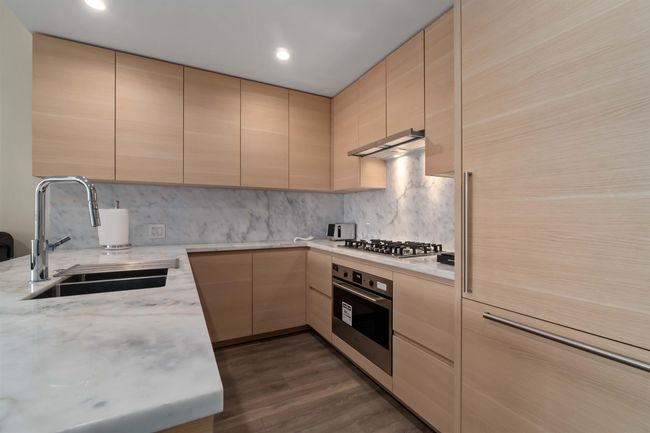 Kitchen featuring wall chimney range hood, a sink, appliances with stainless steel finishes, light brown cabinets, and modern cabinets | Image 13
