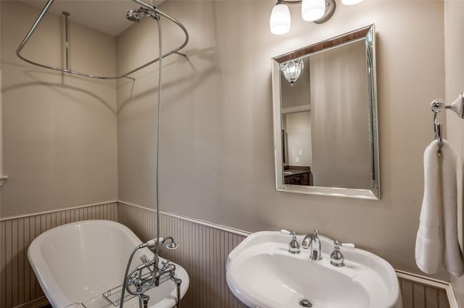 The front bedroom leads to a charming Jack and Jill bathroom featuring a pedestal sink, elegant chandelier, and a classic clawfoot tub with shower. Enjoy beadboard accents and ample storage for towels and laundry. | Image 18