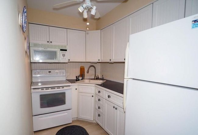 Kitchen featuring white cabinetry, light wood-style flooring, white appliances, a sink, and a ceiling fan | Image 5