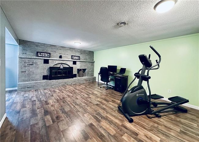 Exercise area with a fireplace, wood finished floors, a textured ceiling, and baseboards | Image 19