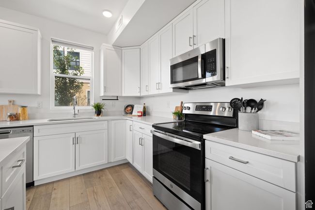 Kitchen featuring appliances with stainless steel finishes, white cabinets, light wood-style floors, and light stone counters | Image 12