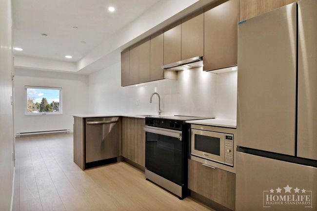 Kitchen with a peninsula, light wood-style floors, baseboard heating, light countertops, and appliances with stainless steel finishes | Image 8