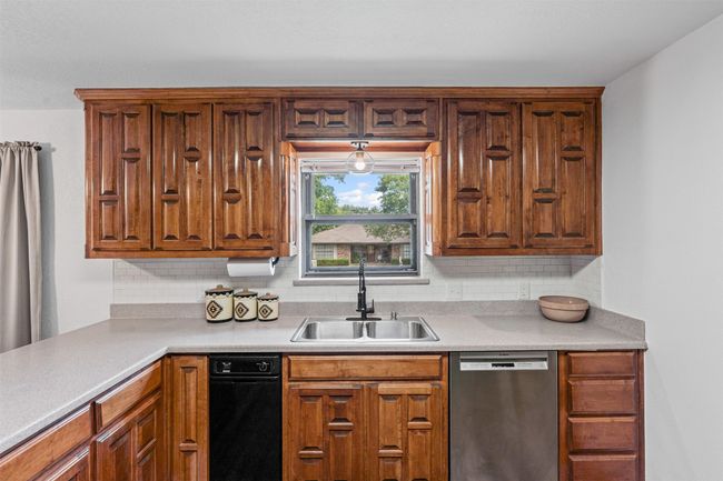 Kitchen featuring stainless steel dishwasher, decorative backsplash, light countertops, and brown cabinetry | Image 12