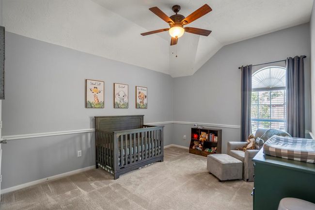 This bright and airy upstairs bedroom boasts a vaulted ceiling, a large window that lets in plenty of natural light, and elegant chair railing. With plenty of space, it’s perfect for creating a cozy retreat or versatile living area. | Image 28