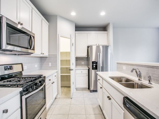 Kitchen with stainless steel appliances, a sink, backsplash, white cabinets, and light tile patterned floors | Image 7