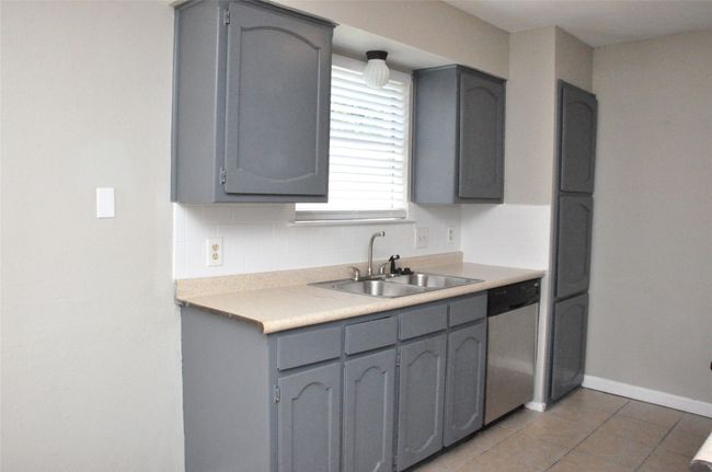 Kitchen with a sink, light tile patterned floors, gray cabinets, backsplash, and dishwasher | Image 12