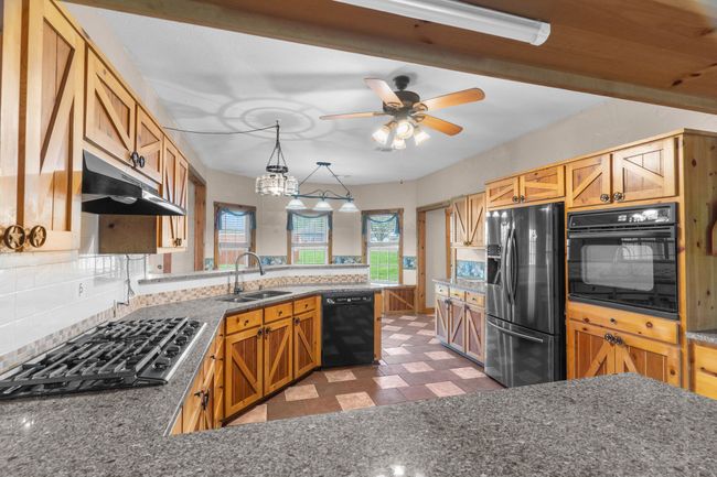 Kitchen featuring tasteful backsplash, a peninsula, black appliances, under cabinet range hood, and a sink | Image 15