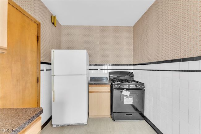 Kitchen with tile walls, wallpapered walls, freestanding refrigerator, and black gas range | Image 14