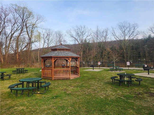 A BBQ area featuring a charcoal grill, tables. lawn, fence, and a gazebo | Image 24