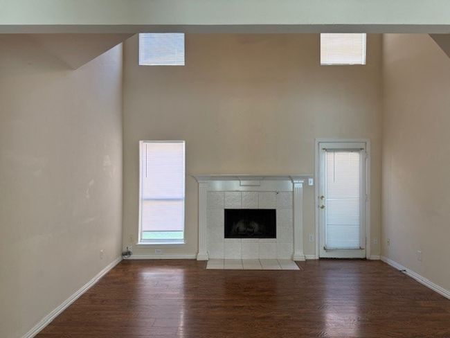 Unfurnished living room featuring wood finished floors, a tile fireplace, and a high ceiling | Image 5