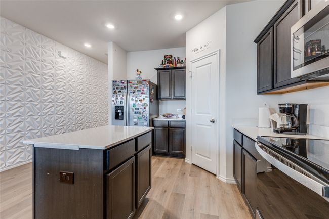 Kitchen with light countertops, stainless steel appliances, dark brown cabinets, a kitchen island, and light wood-style floors | Image 6