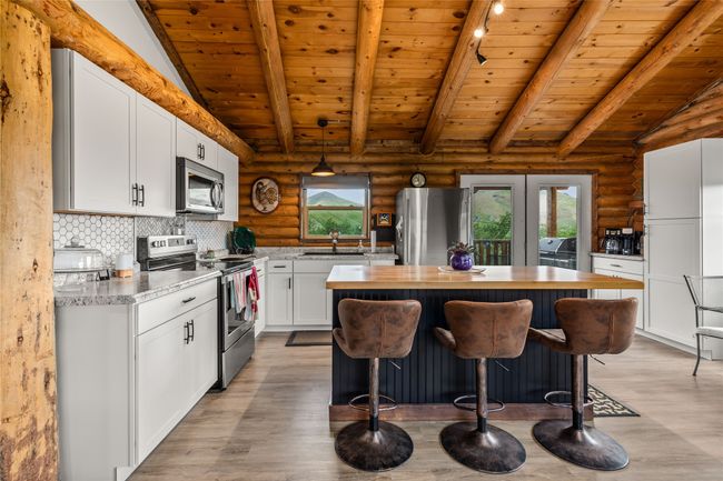 Kitchen featuring stainless steel appliances, rustic walls, healthy amount of natural light, a kitchen island, and light wood-type flooring | Image 6