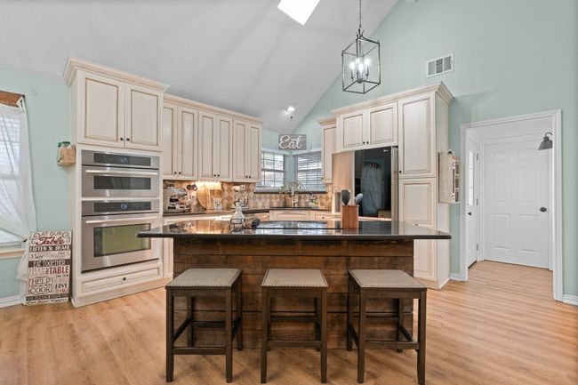 Kitchen with dark countertops, refrigerator, a kitchen breakfast bar, backsplash, and light wood-style flooring | Image 7