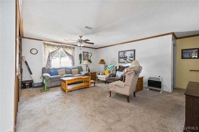 Living area featuring heating unit, a ceiling fan, ornamental molding, a textured ceiling, and carpet flooring | Image 6