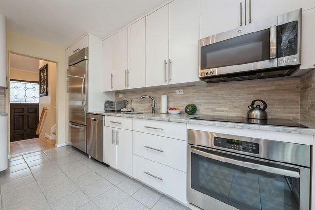 Kitchen with decorative backsplash, white cabinetry, a sink, and appliances with stainless steel finishes | Image 8