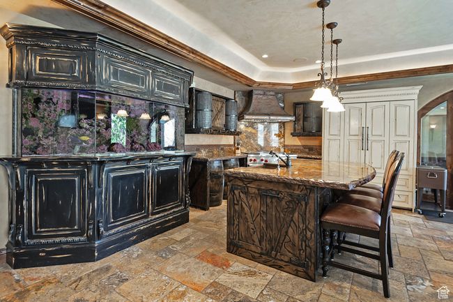 Kitchen with premium range hood, stone tile flooring, dark stone counters, a raised ceiling, and pendant lighting | Image 51